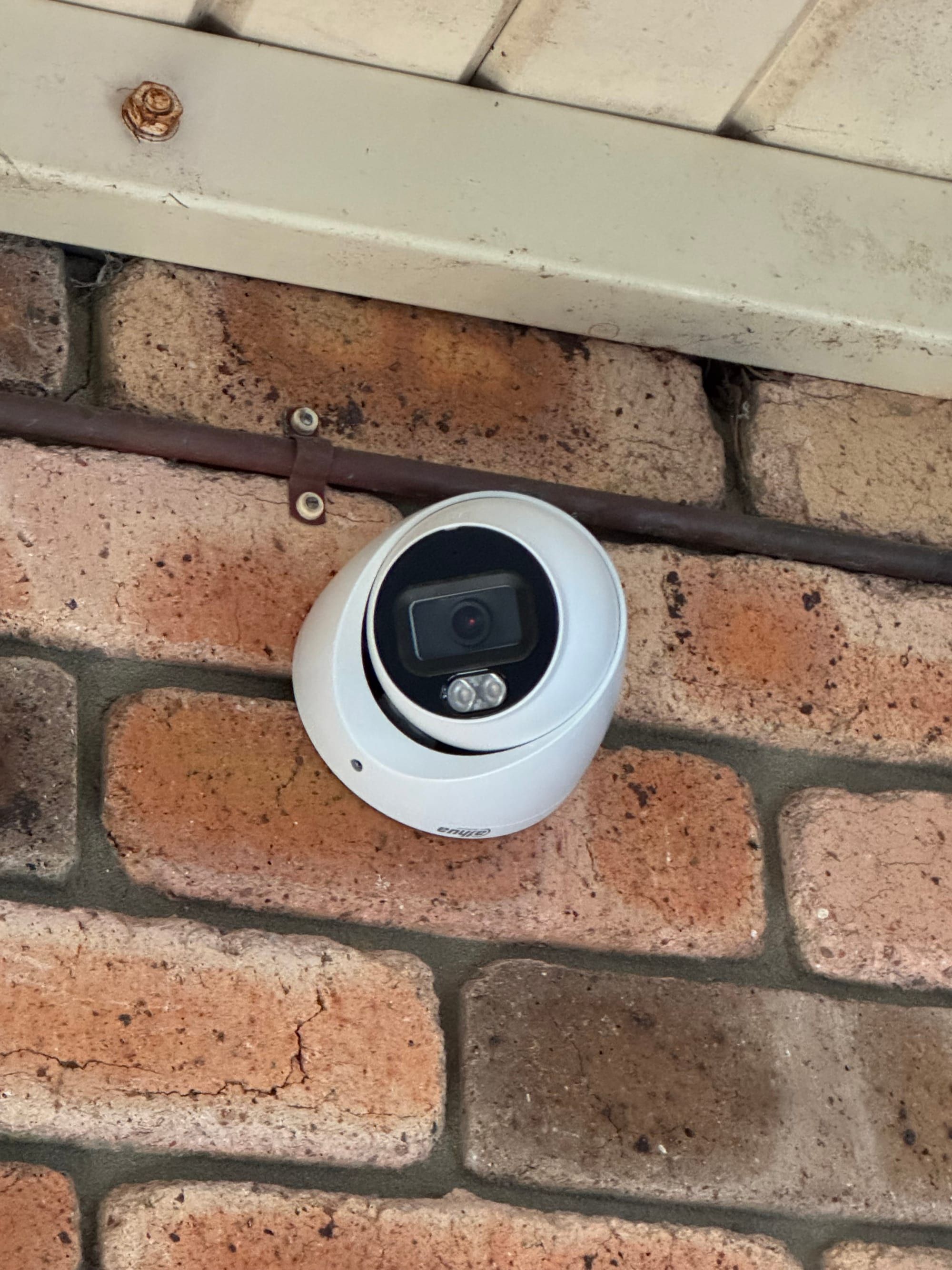 Dome security camera installed under an eave on a brick home